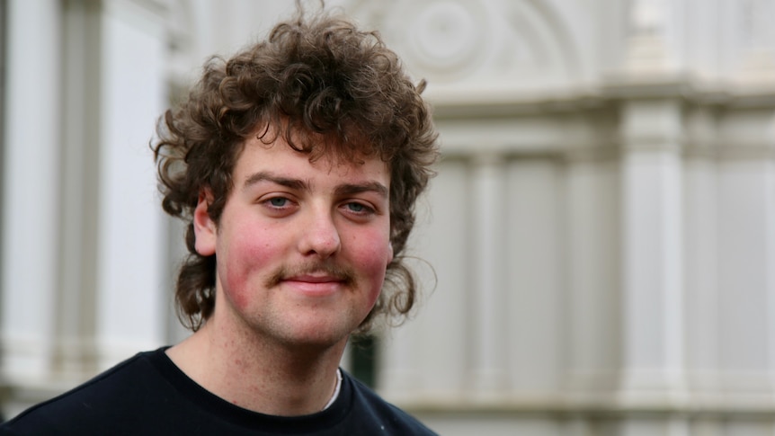 A man with curly hair and a moustache smiling.