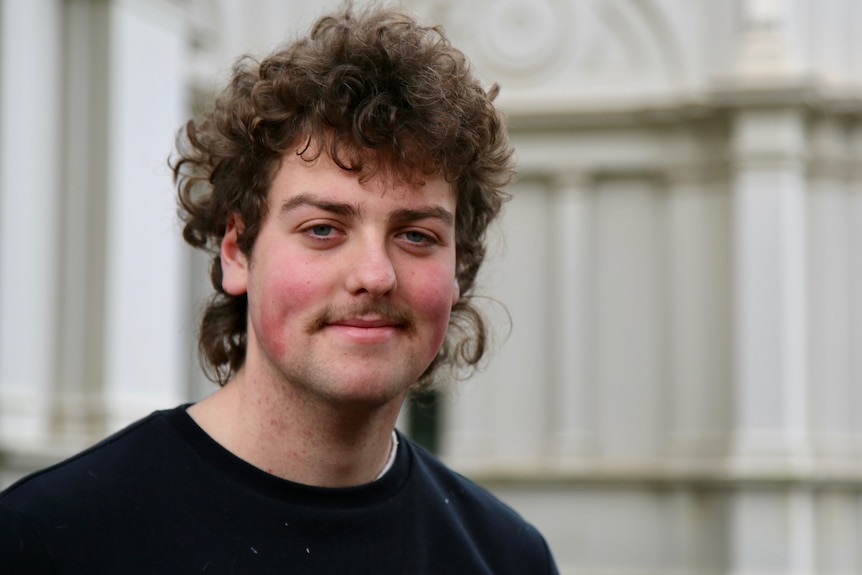 A man with curly hair and a moustache smiling.