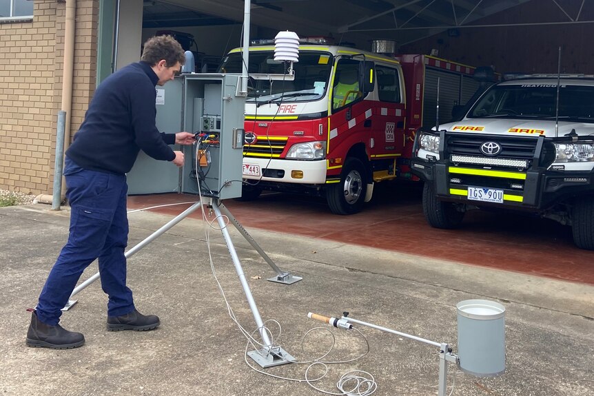 A man setting up a weather station that looks like a power box on a stick 
