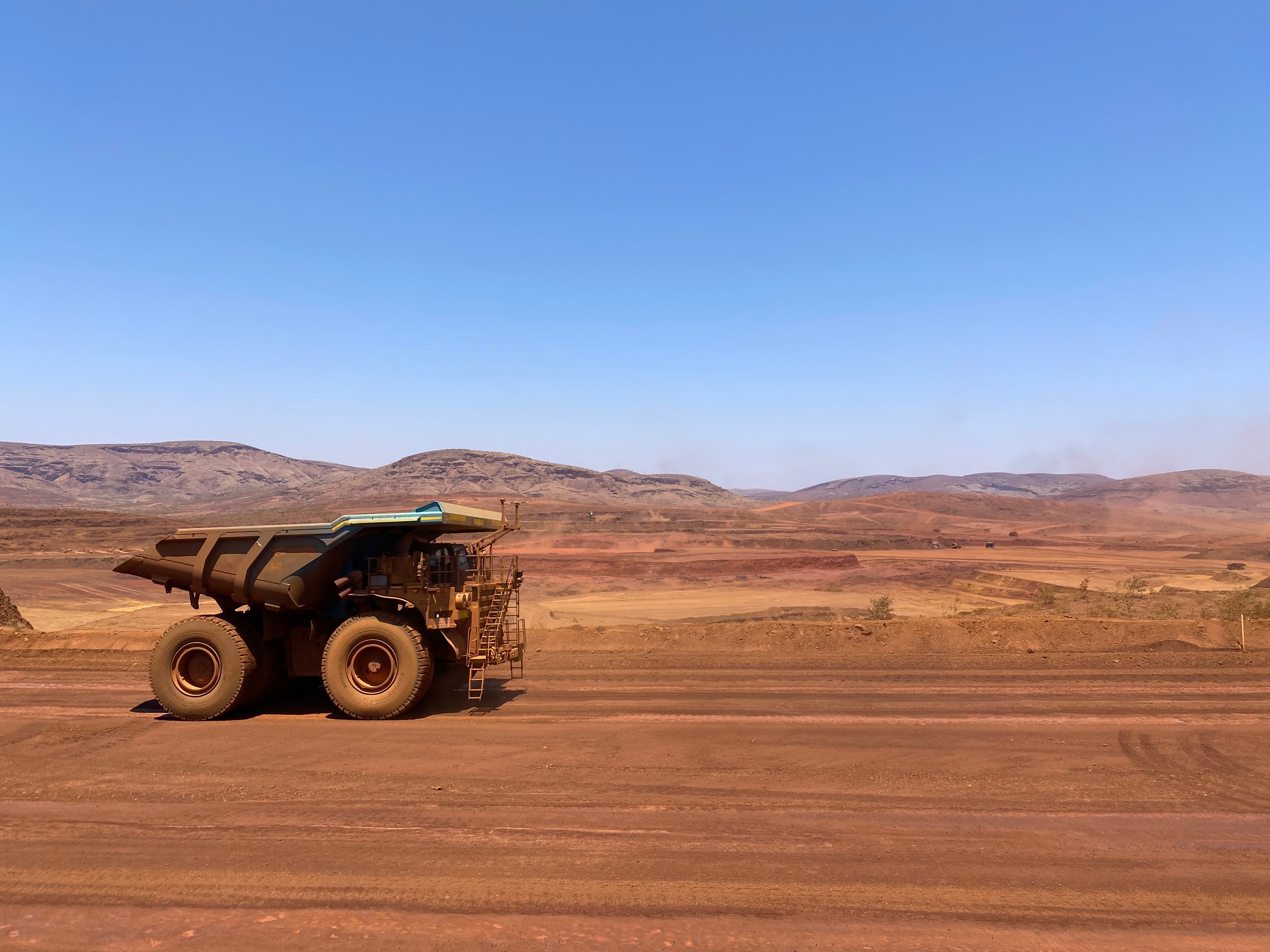 A dump truck drives along red dirt near a mine