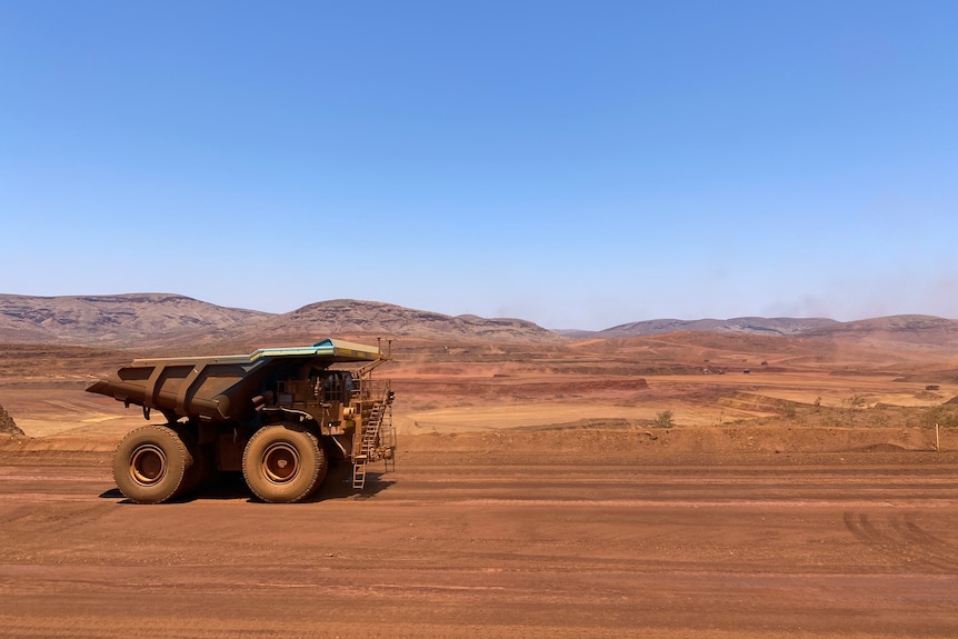 A dump truck drives along red dirt near a mine