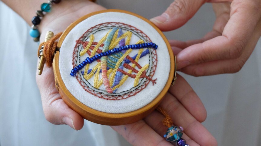 Circular needle point picture of astrolabe, held by Keshira haLev Fife.