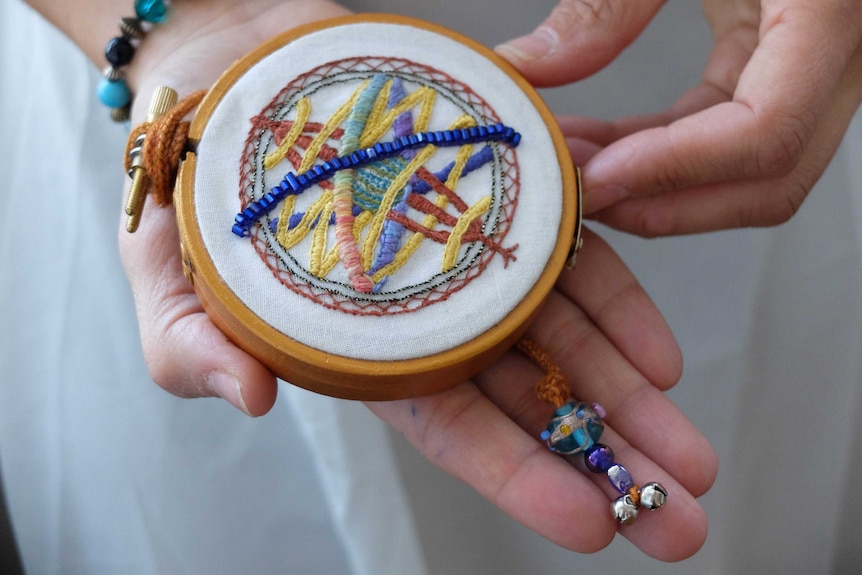 Circular needle point picture of astrolabe, held by Keshira haLev Fife.