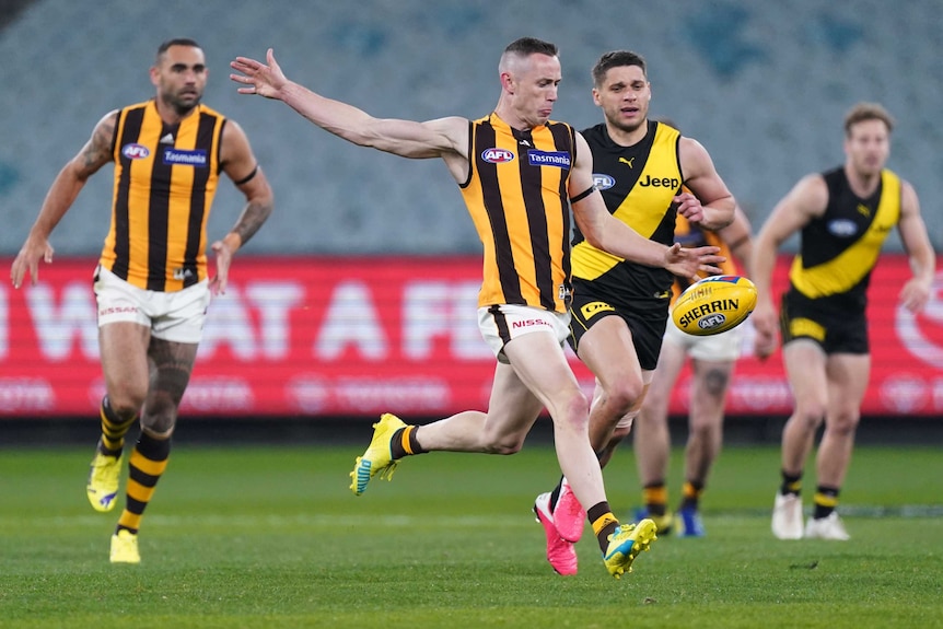 A Hawthorn AFL player kicks the ball against as he is being chased by a Richmond player at the MCG.