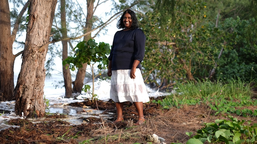 Woman standing under a tree as a high tide washes close to her feet.