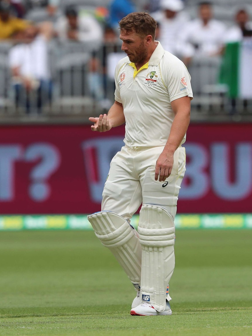 Aaron Finch walks from the field holding out his injured finger.
