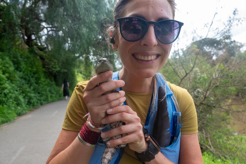 A woman smiles as she holds a lizard.