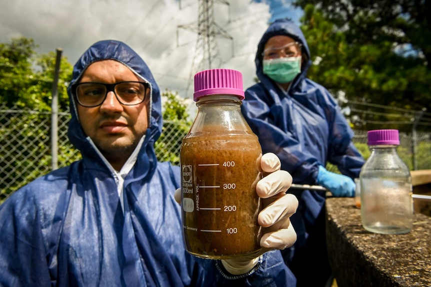 Ali Khalid holds a jar with a sewage sample inside.