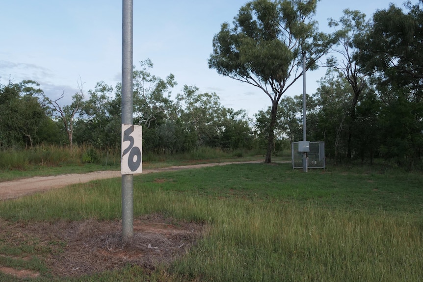 Il cartello temporaneo dice "50" All'esterno di un fitto isolato rurale.  Sullo sfondo c'è un'alcova circondata da una gabbia. 