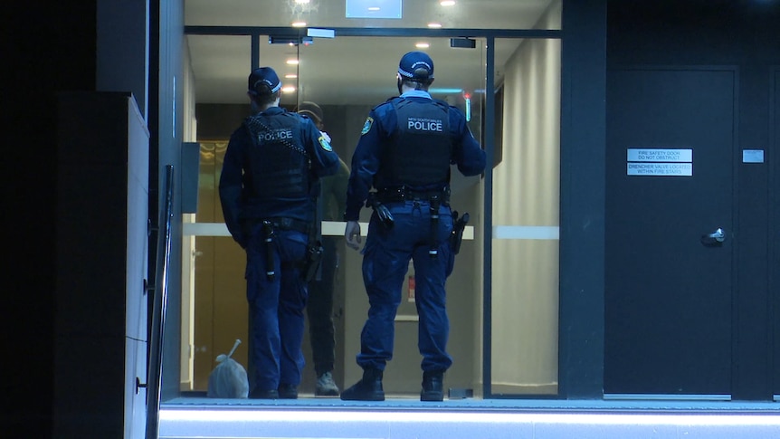 police officers speak to man behind glass automatic doors