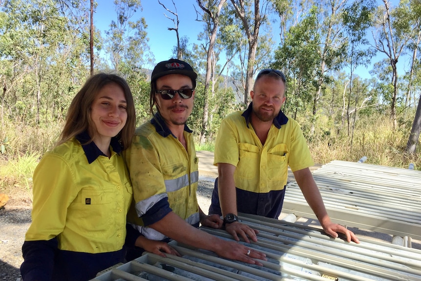 A woman and two men look at mine drill core samples. 
