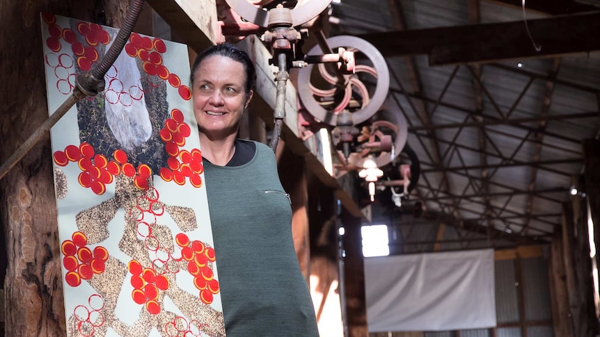 A woman with an abstract artwork standing in an old shearing shed