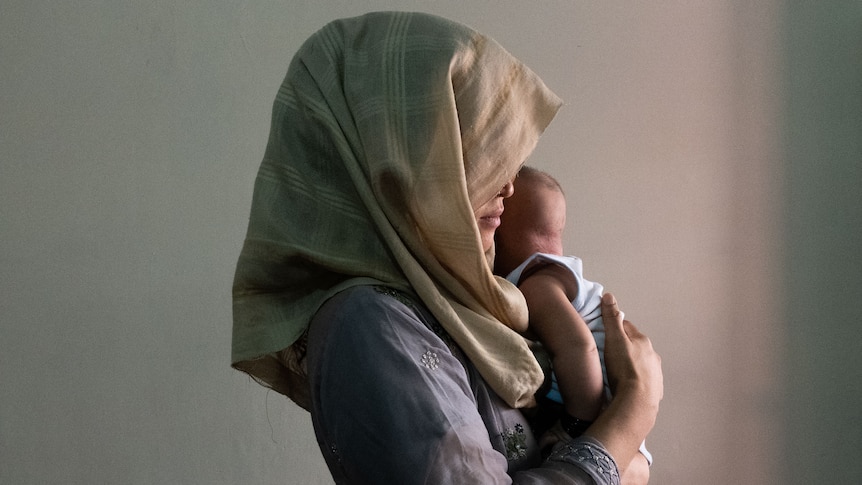 A woman in a headscarf holds a small child close to her chest. 