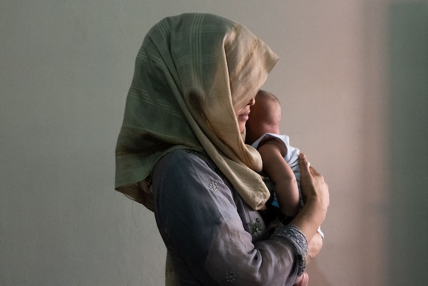 A woman in a headscarf holds a small child close to her chest. 