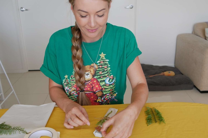 A woman sits at a table wrapping Christmas gifts.