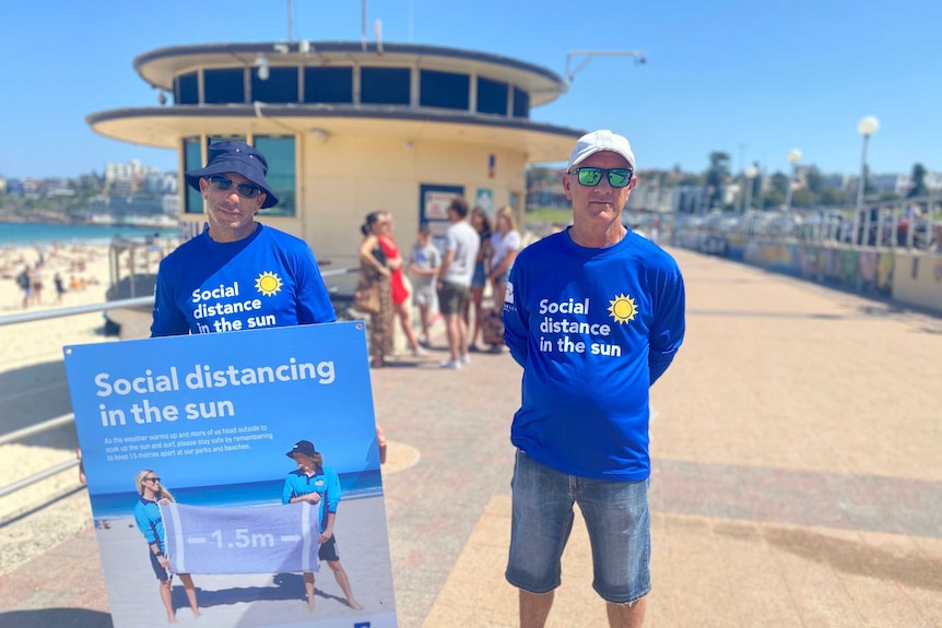 Two men holding a sign that says 'social distancing in the sun'