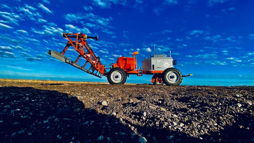 a red tractor liike machine with a spray boom at the back viewed from spoil level and looking at blue sky.