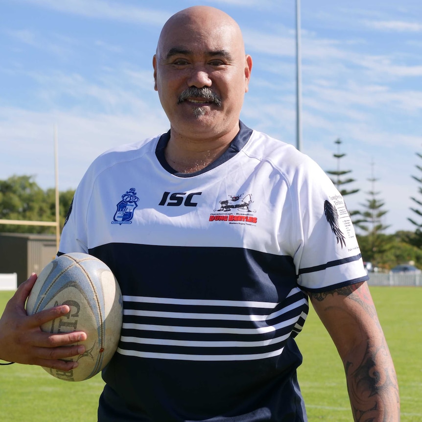 A man with a rugby jersey holding a rugby union ball outside on a rugby field.