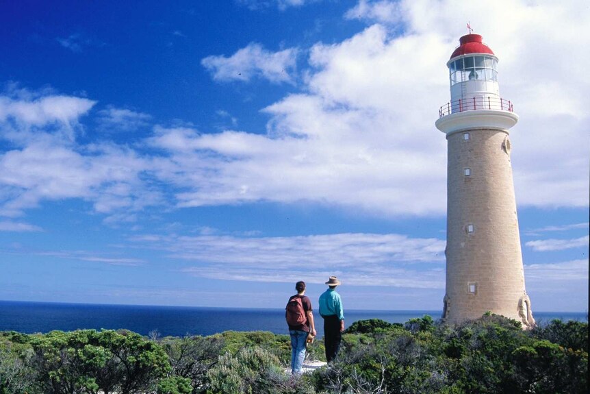 Two people walk up to a tall thin white lighthouse