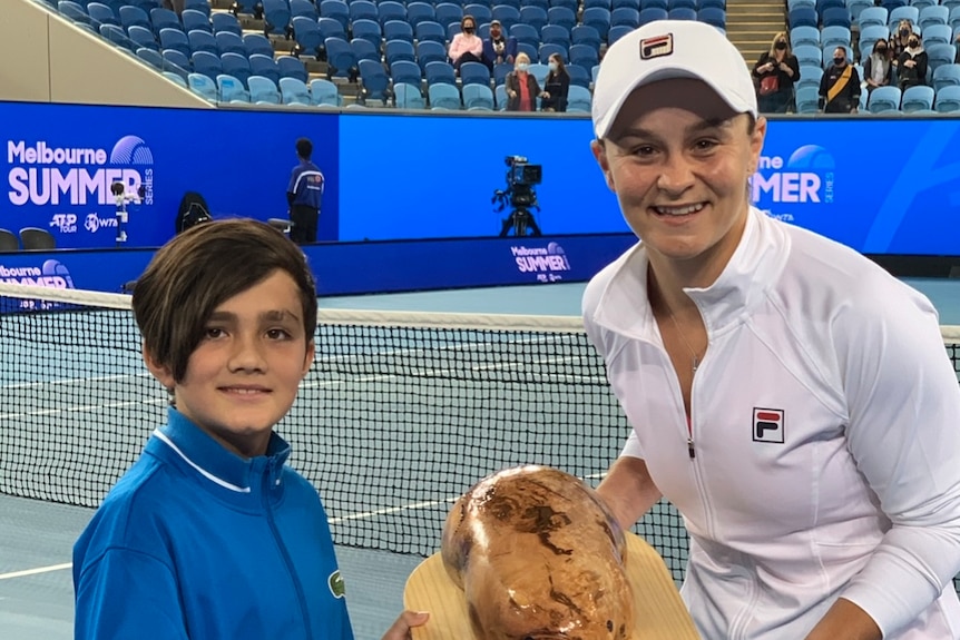 A young kid giving a wombat-shaped trophy to Ash Barty, a female tennis player.