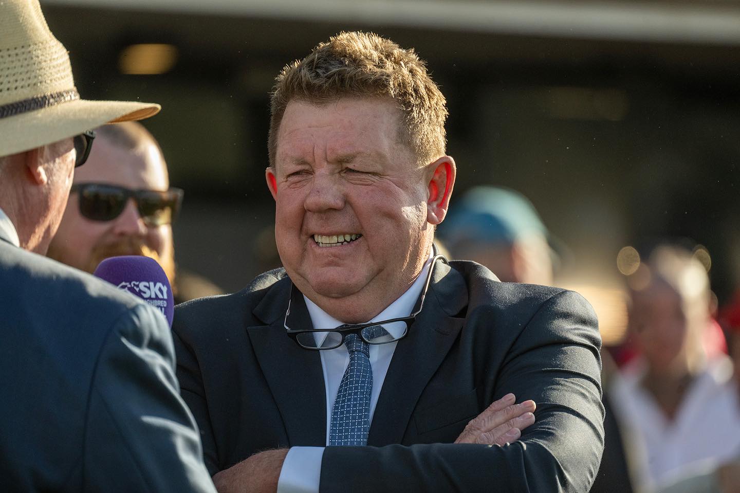 A man in a suit stands with his arms crossed, smiling.