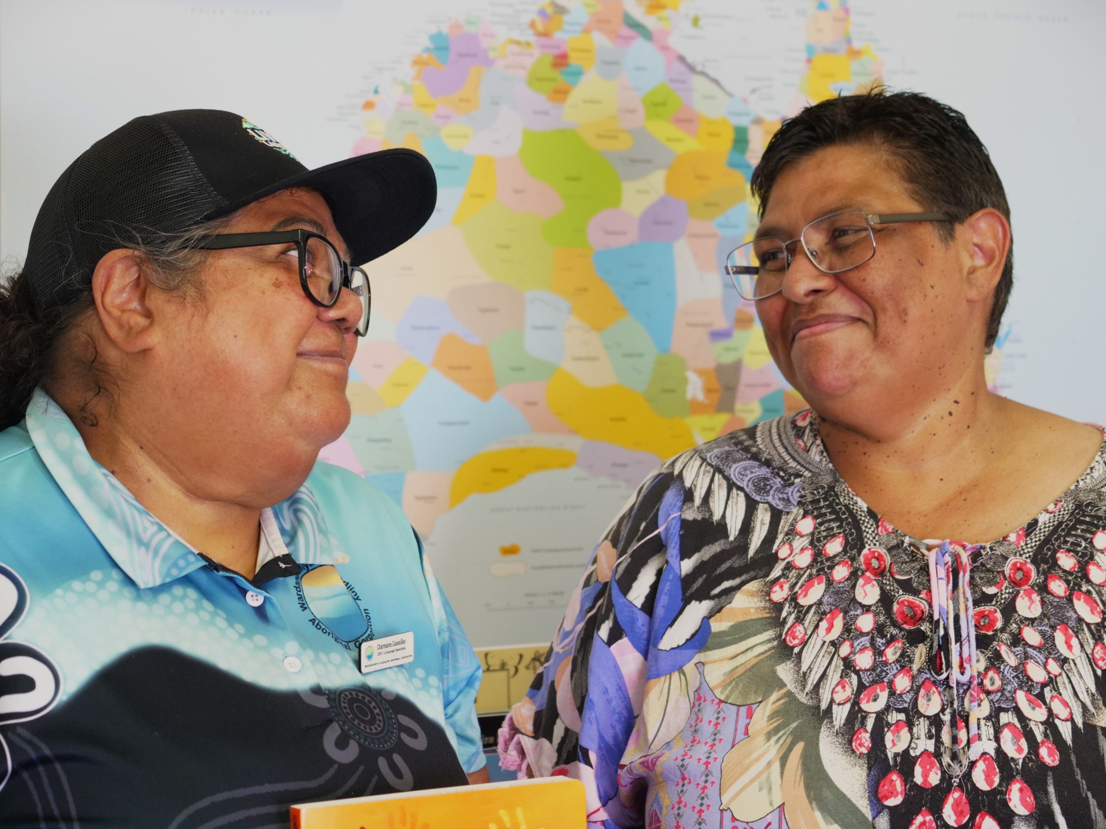 Dos mujeres mayores se miran fijamente frente a un colorido mapa de Australia.