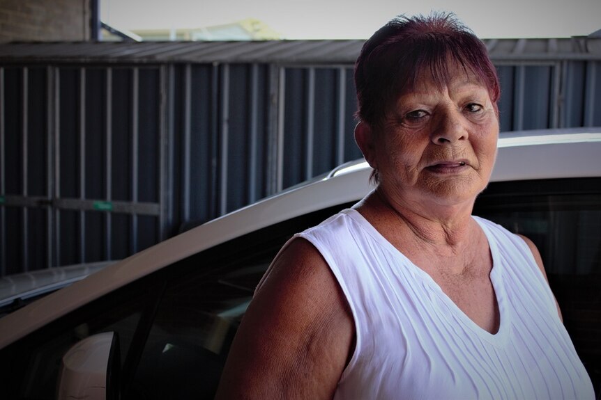 Middle-aged Bundjalung woman stands next to a car.