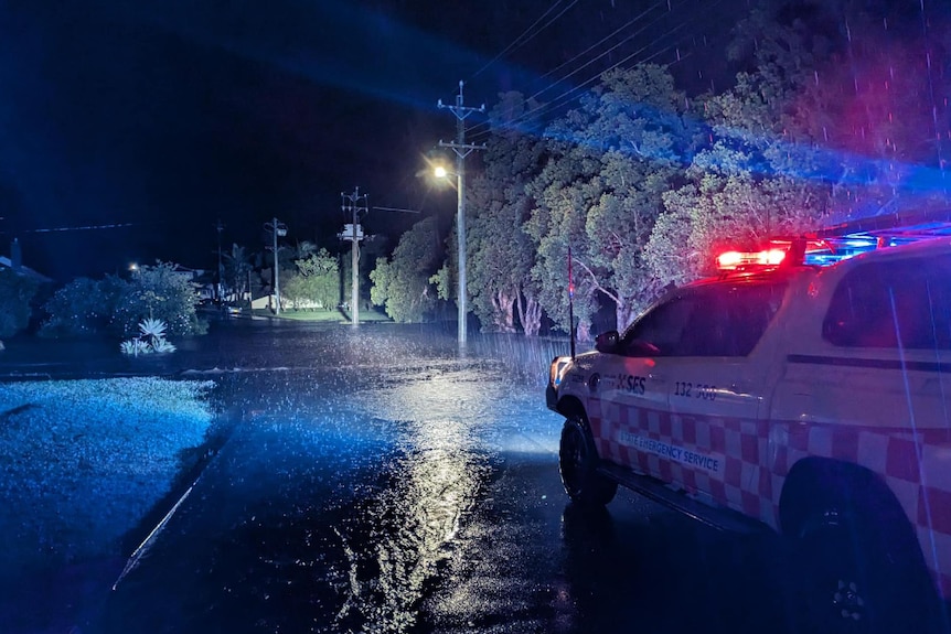 Rain falls on flooded road, SES vehicles with lights on.