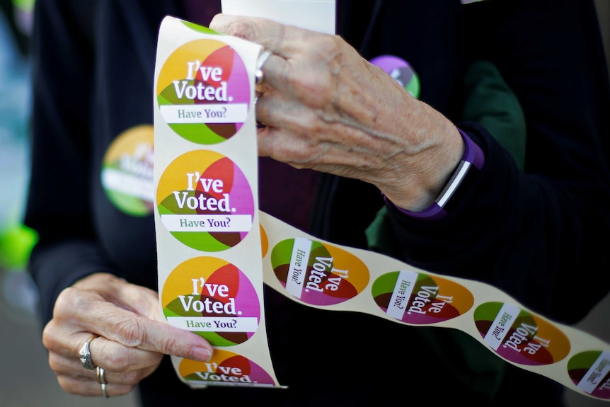 A woman holds sheet of stickers that read "I've voted, have you".