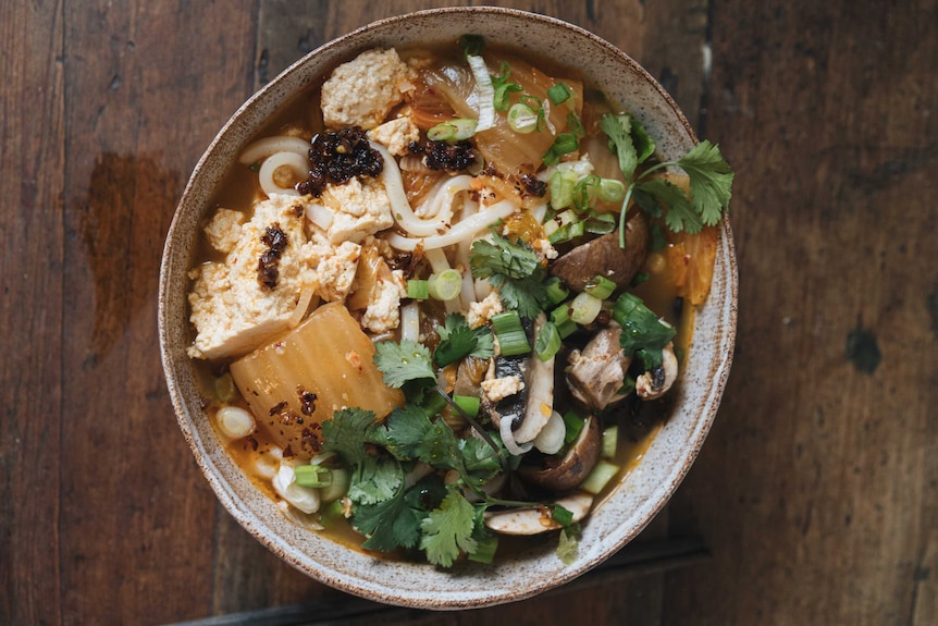 A bowl of spicy noodle soup with udon noodles, tofu, kimchi, spring onions, coriander, cooking during coronavirus.