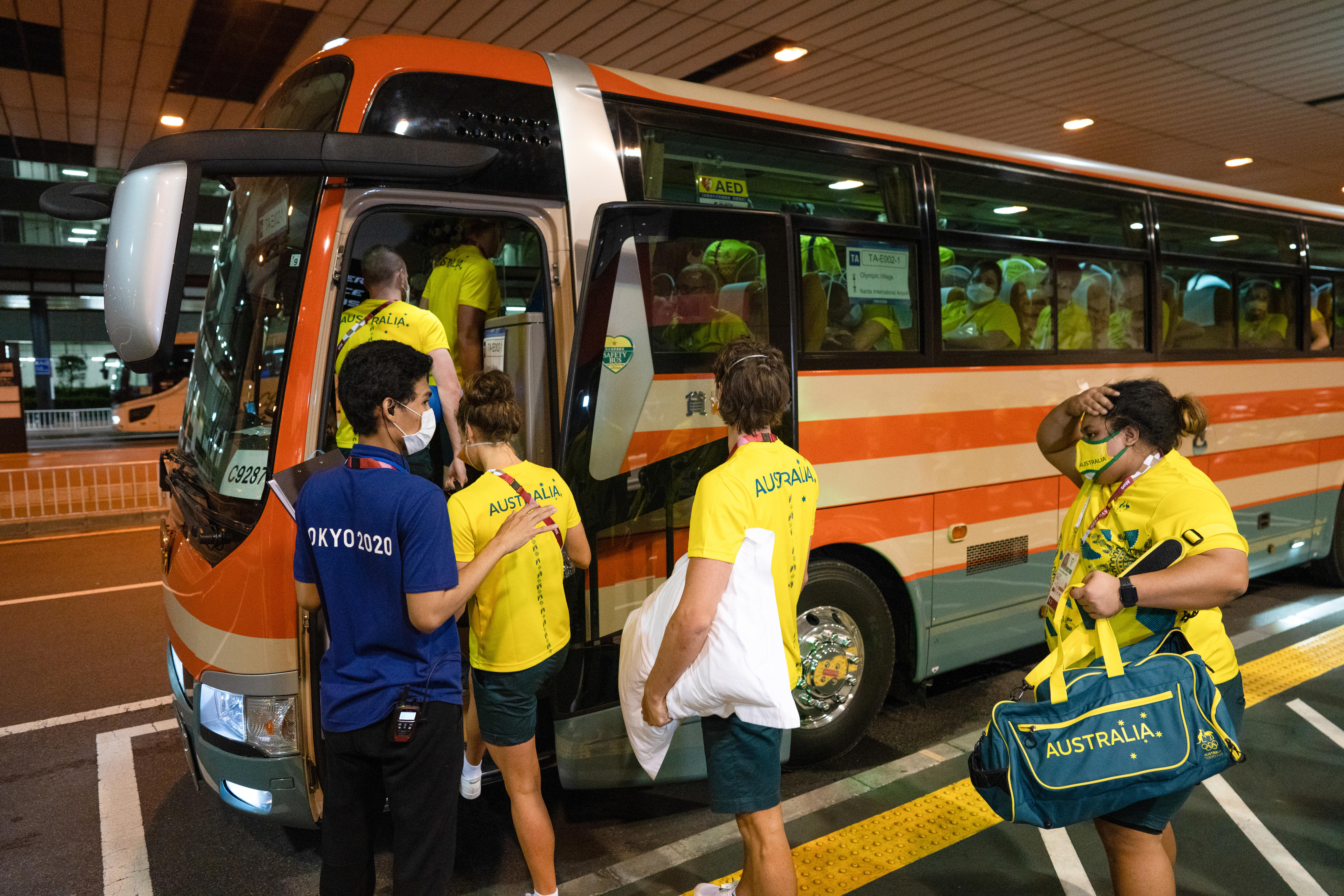 People in yellow jerseys and green shirts line up to board a bus 