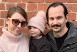 Shannon, Isla and Chris Pierucci stand together in front a red brick wall. They wear winter attire.