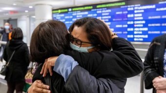 Travellers wearing face masks embracing in an airport