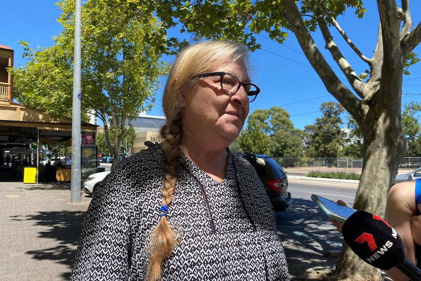 A woman with a long plait in her hair stands side on during a conversation