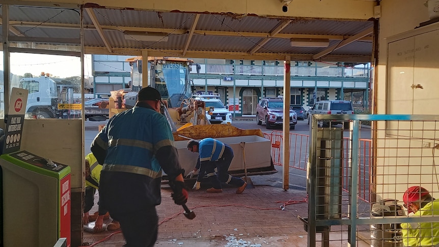 Workers repairing damage to a supermarket entrance after a ram raid. 