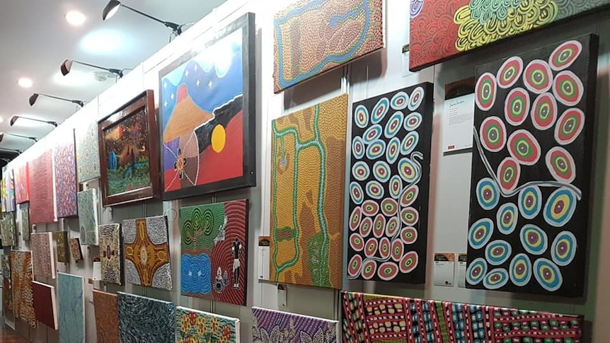 Various colourful Indigenous paintings on a wall.