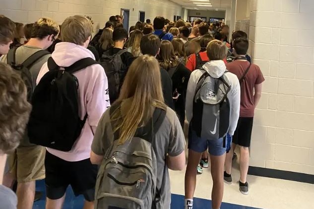 A shot of the backs of a group of teenagers crowded into a school hallway.