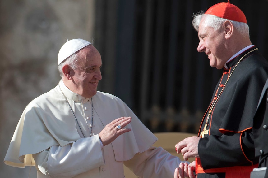 Pope Francis, dressed in all white, speaks with Cardinal Mueller who is wearing black robes and a red zucchetto.