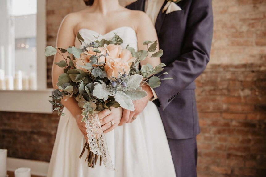 Bride holding flowers, and groom, faces obscured.