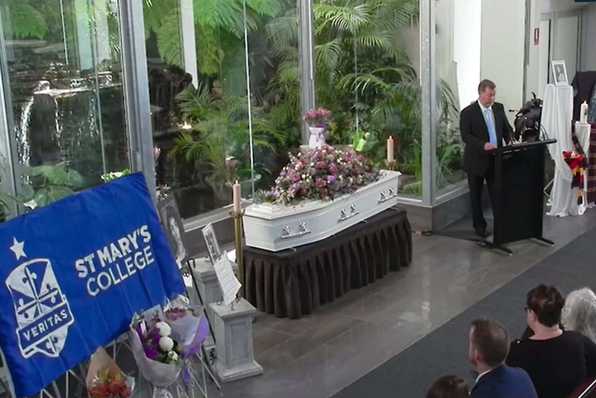 Greg Ireland speaks at a podium beside his daughter's coffin