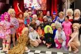 a group of people in colourful clothing, including drag queens wearing multicoloured wigs.