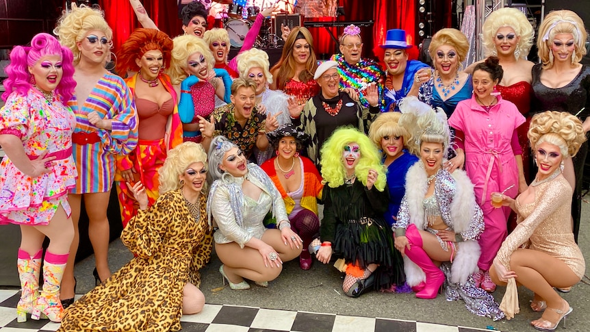 a group of people in colourful clothing, including drag queens wearing multicoloured wigs.