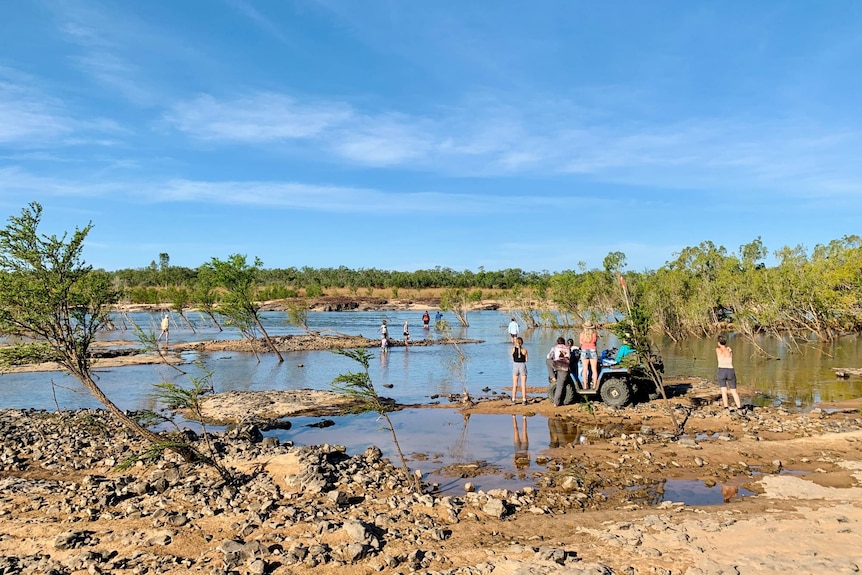 People stand around a quad bike near a wide stretch of water.