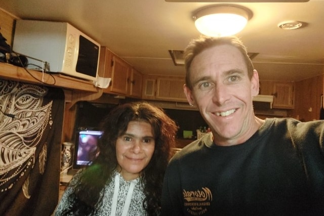 A man smiling at a camera with a woman in a caravan.
