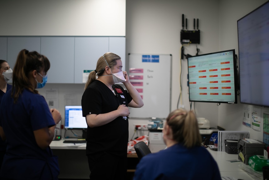 Midwives in a staffroom, looking up a screen near the rosters.