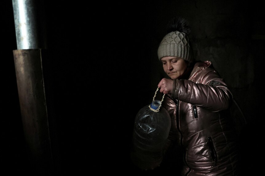 a woman wearimg a beanie and a jacket in a dark room pours water into a pot 