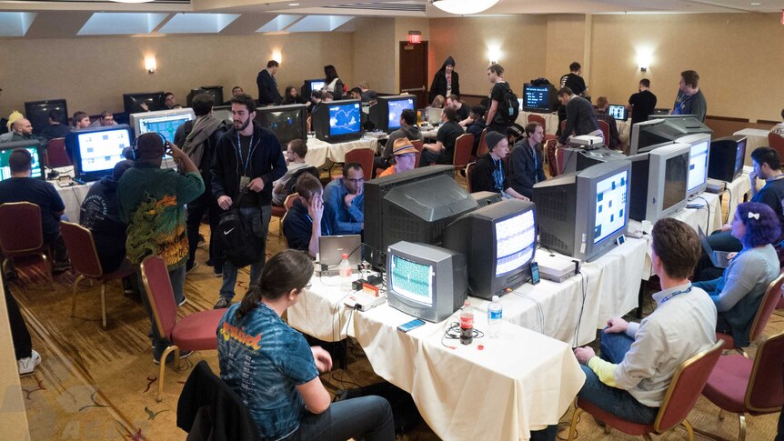 People sit in a room with many televisions and videogame consoles