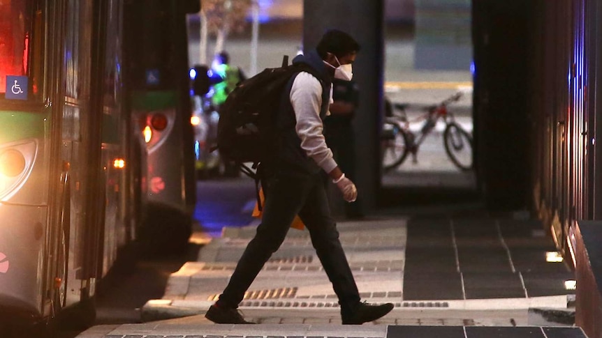 A live export ship crew member with a backpack and face mask on walks away from a Transperth bus at dusk towards a hotel.