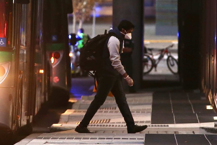 A live export ship crew member with a backpack and face mask on walks away from a Transperth bus at dusk towards a hotel.