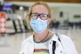 Ms Mardling wears a mask and stands in the airport terminal.